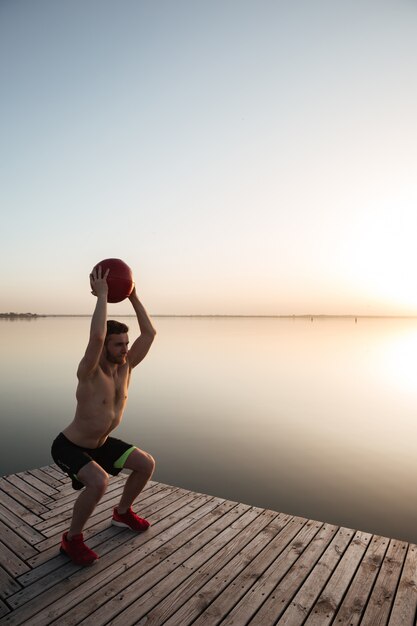 De ernstige jonge sportman maakt sportoefeningen met bal