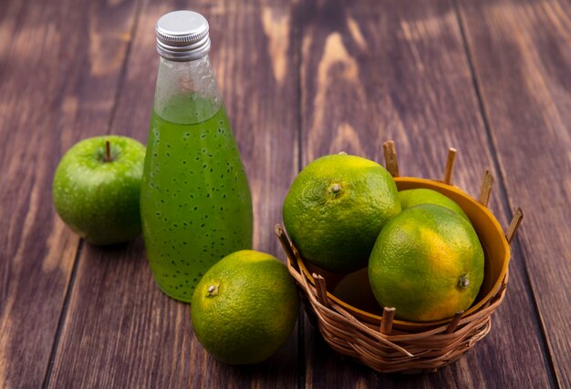 De fles van het vooraanzichtsap met mandarijnen in mand en appel op houten muur