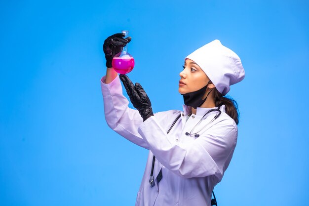 De geïsoleerde verpleegster in hand en gezichtsmasker houdt chemische kolf vast en kijkt zorgvuldig