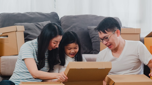 De gelukkige Aziatische jonge verhuizingen van de familieverplaatsing regelen in nieuw huis. Chinese ouders en kinderen openen kartonnen doos of pakket uitpakken in de woonkamer op verhuisdag. Onroerend goed woning, lening en hypotheek.