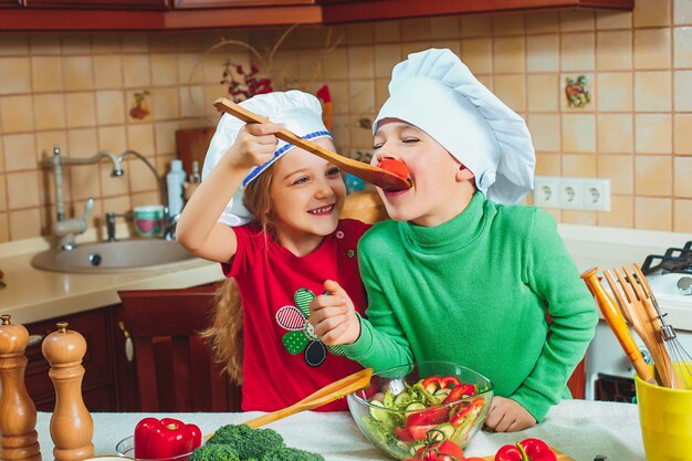 De gelukkige familie grappige jonge geitjes bereiden verse groentesalade in de keuken voor