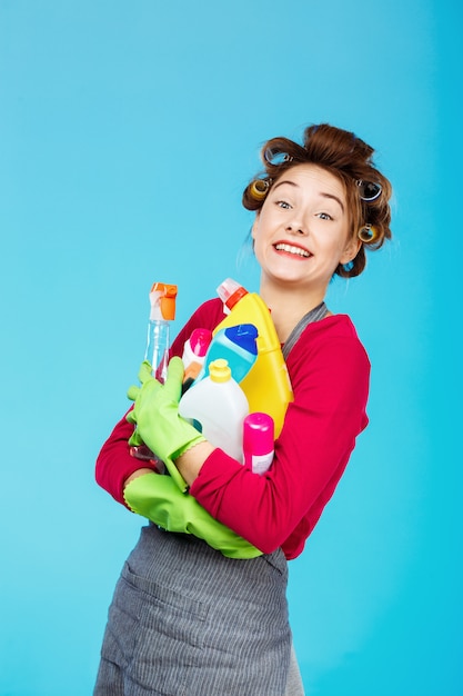 De gelukkige huisvrouw houdt schoonmakende hulpmiddelen dragend groene handschoenen