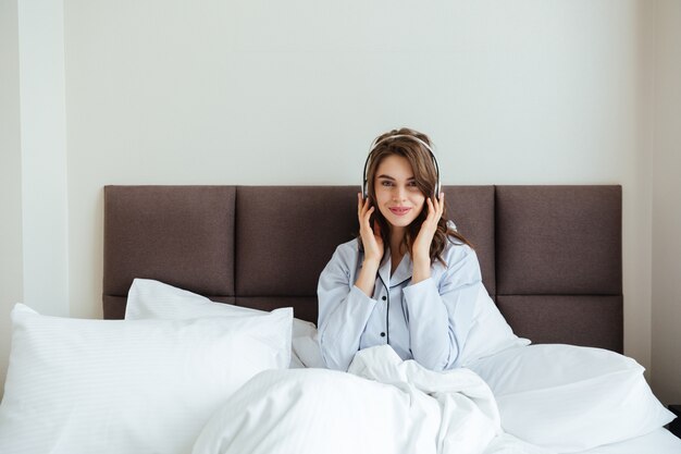 De gelukkige jonge dame ligt in bed thuis het luisteren muziek.