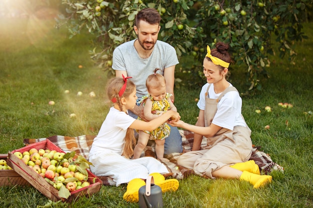 De gelukkige jonge familie tijdens het plukken appels in een tuin buitenshuis