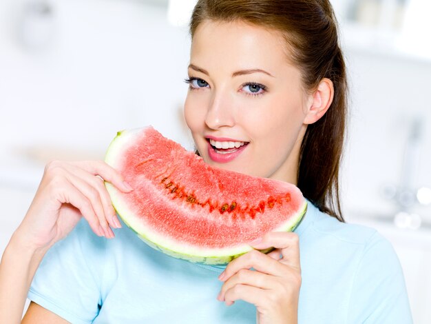 De gelukkige jonge vrouw eet een rode watermeloen