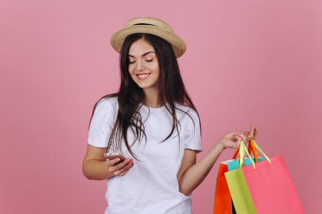 De gelukkige jonge vrouw gebruikt haar telefoon die met kleurrijke het winkelen zakken in de studio stelt