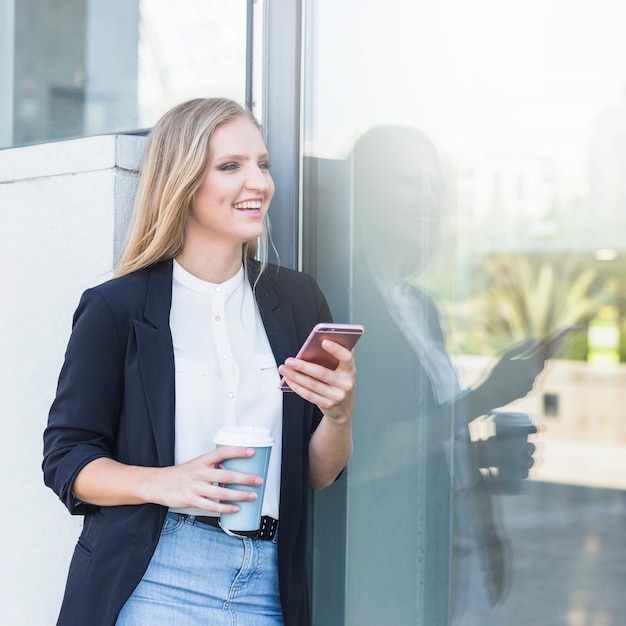 De gelukkige jonge vrouwenholding haalt koffiekop weg gebruikend cellphone