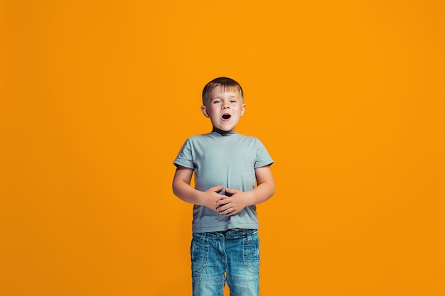 De gelukkige jongen die en zich tegen oranje muur bevindt glimlacht