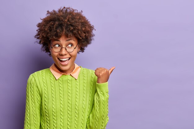 De gelukkige knappe etnische vrouw met Afro-haar wijst weg op lege ruimte