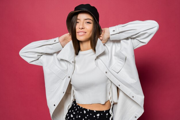 De gelukkige leuke haren van de vrouwenholding op roze achtergrond. Gelukkig vrouw in witte jas en zwarte trendy panama poseren in studio.