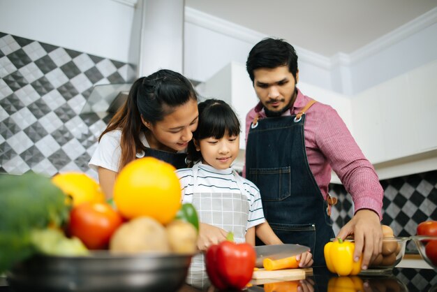 De gelukkige mama onderwijst haar dochter die groente hakt die ingrediënten voorbereidt