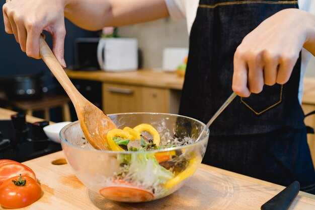 De gelukkige mooie Aziatische vrouw bereidt saladevoedsel in de keuken voor