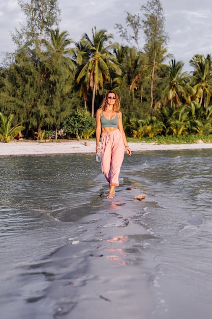 De gelukkige mooie jonge Europese vrouw met plastic fles water in haar dient het strand in