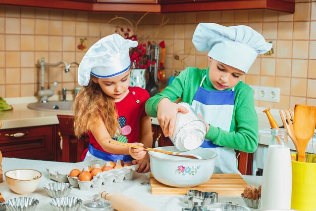 De gelukkige twee grappige kinderen bereiden het deeg voor, bakken koekjes in de keuken