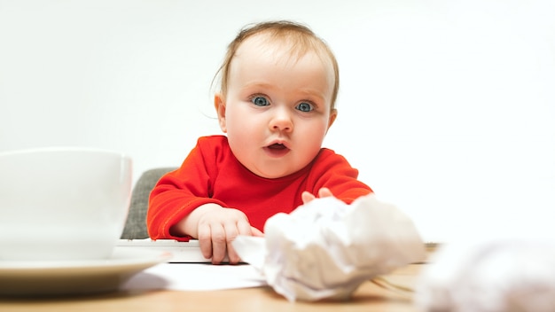 De gelukkige zitting van de het meisjespeuter van de kindbaby met toetsenbord van computer die op een wit wordt geïsoleerd