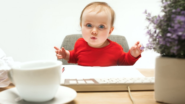 De gelukkige zitting van de het meisjespeuter van de kindbaby met toetsenbord van computer die op een witte achtergrond wordt geïsoleerd