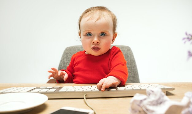 De gelukkige zitting van de het meisjespeuter van de kindbaby met toetsenbord van de computer die op een wit wordt geïsoleerd