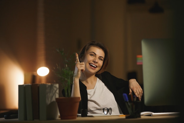 De gelukkige zitting van de jonge dameontwerper in bureau bij nacht