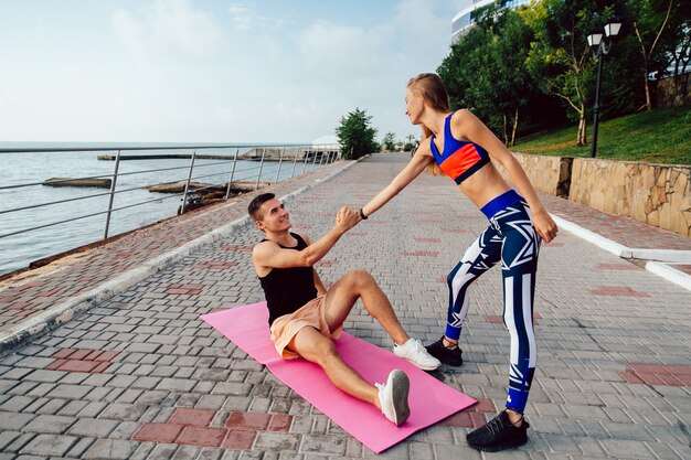 De geschiktheidsvrouw helpt een gelukkige sportman om op te staan ​​na het doen van een sportoefening