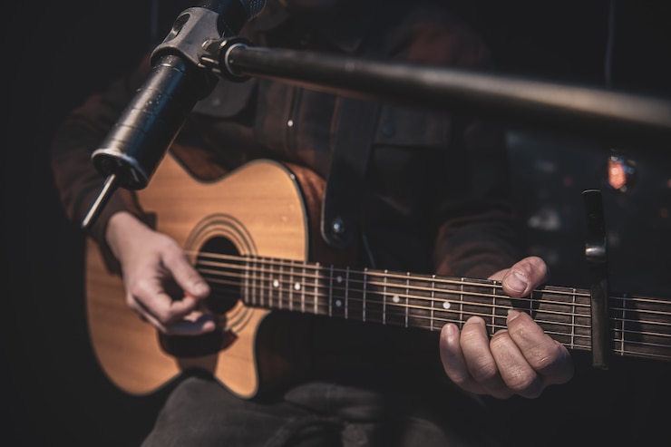 Gratis Foto de gitarist speelt een akoestische gitaar met een capo voor een microfoon
