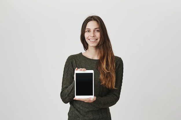 De glimlachende gelukkige jonge vrouw die het digitale tabletscherm tonen, adverteert app of winkel