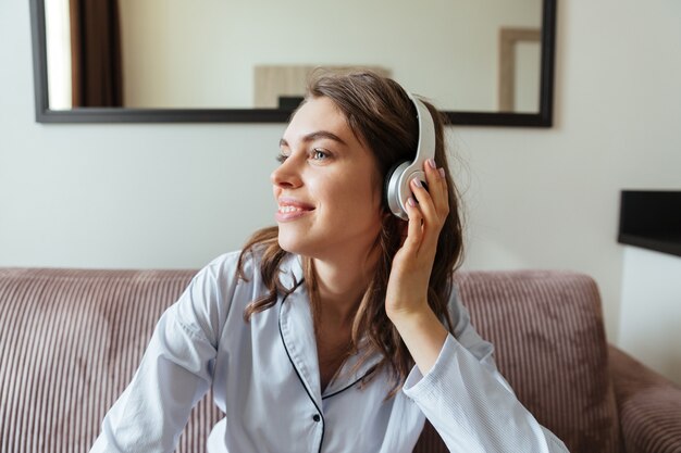 De glimlachende jonge dame kleedde zich in pyjama het luisteren muziek