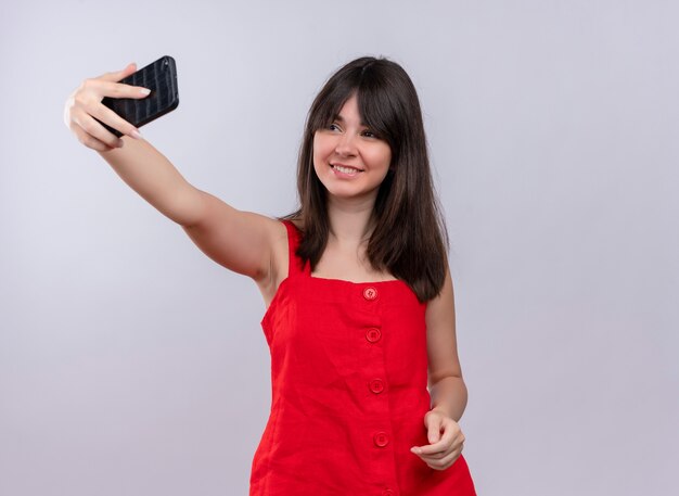 De glimlachende jonge Kaukasische telefoon van de meisjesholding en het bekijken telefoon op geïsoleerde witte achtergrond