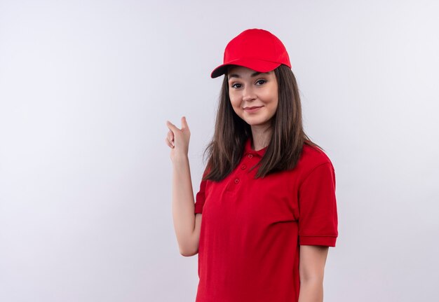 De glimlachende jonge leveringsvrouw die rode t-shirt in rood GLB draagt wijst naar rug op geïsoleerde witte muur