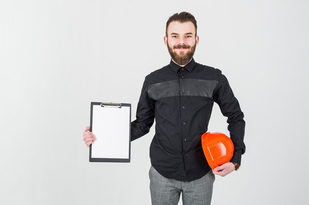 De glimlachende jonge mannelijke bouwvakker en het klembord van de architectenholding