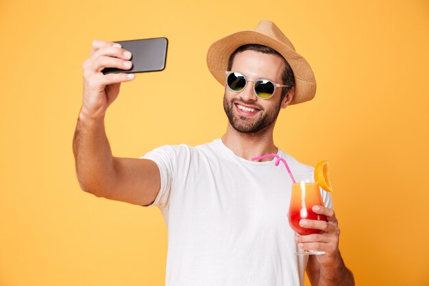 De glimlachende jonge mens maakt selfie telefonisch holdingscocktail.