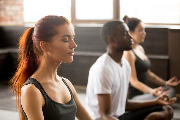 De groep jonge sportieve mensen in Sukhasana, sluit omhoog