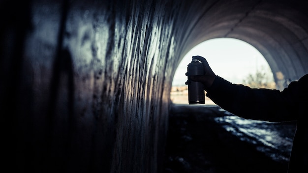 De hand die van de kunstenaar graffiti met spuitbus in tunnel schildert