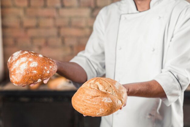 De hand die van de mannelijke bakkers geheel gebakken brood houdt