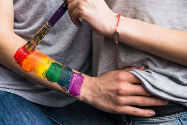 De hand die van de vrouw de regenboogvlag over de hand van het meisje met penseel schildert