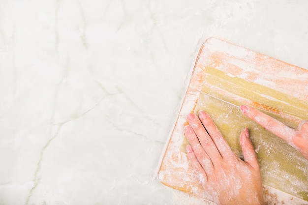 De hand die van de vrouw deegwaren op hakbord voorbereidt