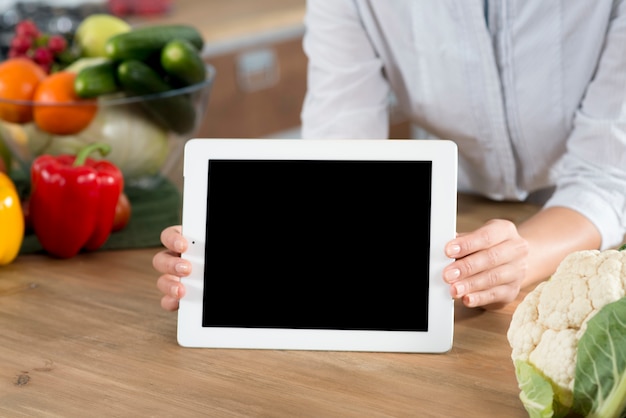 De hand die van de vrouw digitale tablet met het lege scherm op houten keukenteller houdt