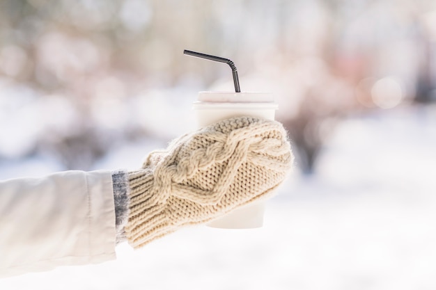 De hand die van de vrouw handschoenen draagt ​​die beschikbare koffiekop in de winter houden