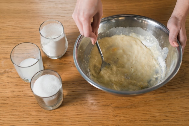 De hand die van de vrouw het het bakseldeeg in de roestvrije kom mengt