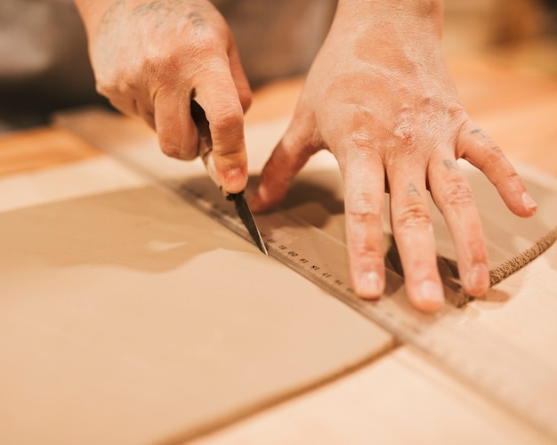 De hand die van de vrouwelijke pottenbakker de klei met scherp hulpmiddel snijdt