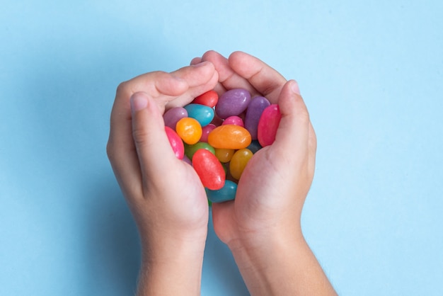 De hand die van het kind verscheidene Jelly Beans over blauwe oppervlakte houdt