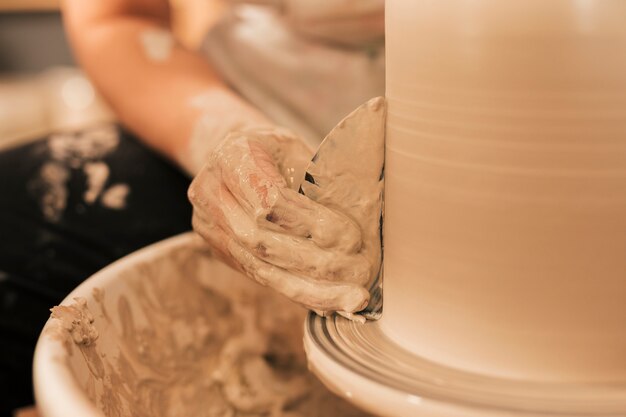 De hand die van het wijfje vaas met vlak hulpmiddel op het wiel van pottenbakkers gladmaakt