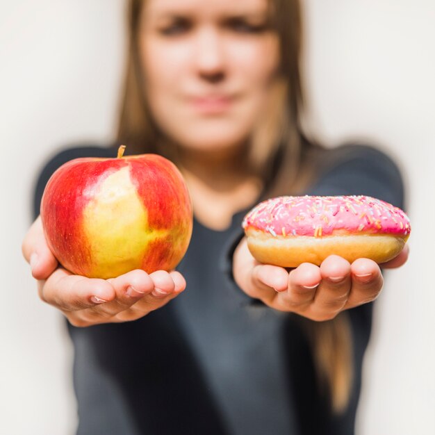 De hand die van het wijfje verse appel en doughnut houdt