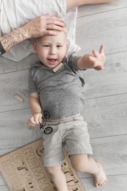 De hand van de moeder op het hoofd van de kleine zoon die op de hardhouten vloer ligt die zijn hand opheft