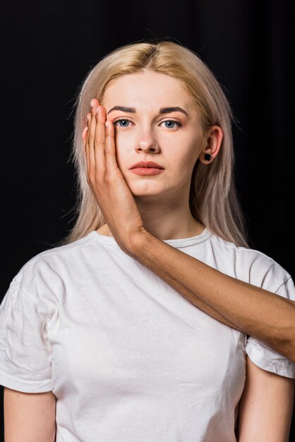 De hand van de vriend op de wang van de blonde jonge vrouw tegen zwarte achtergrond