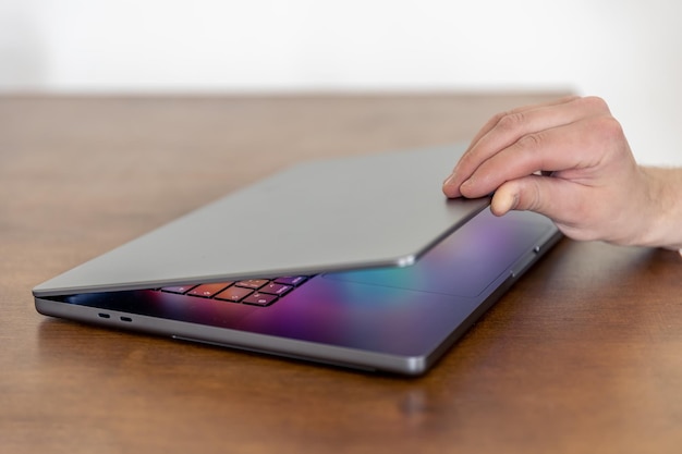 De hand van een man opent een laptop met een veelkleurig gloeiend scherm
