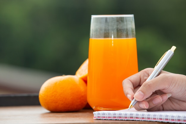 De hand van het meisje dat een boek met jus d'orange en sinaasappelen schrijft