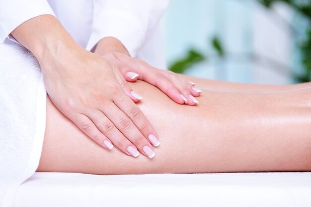De handen van de schoonheidsspecialiste die massage voor het vrouwelijke been doen