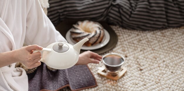 De handen van een jonge vrouw schenken thee uit een theepot.