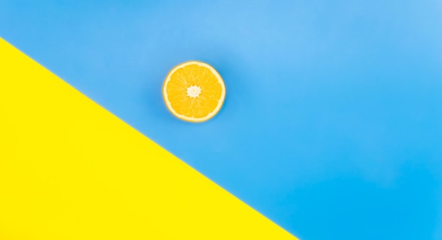 Gratis foto de helft van een sinaasappel op een blauwe en gele achtergrond lag plat minimalisme