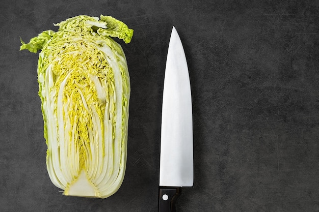 De helft van Peking-kool op een grijze tafel, naast een koksmes, kooksalade. Bovenaanzicht met kopieerruimte